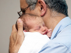 Far holder sitt nyfødte barn tett inntil kroppen og koser