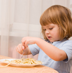 Liten jente ruller spaghetti opp på gaffelen