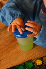 Små barnehender med vannglass for å dyppe malepenselen