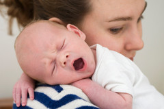 Liten baby gjesper på skulderen til mamma