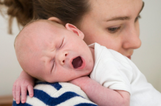 Liten baby gjesper på skulderen til mamma